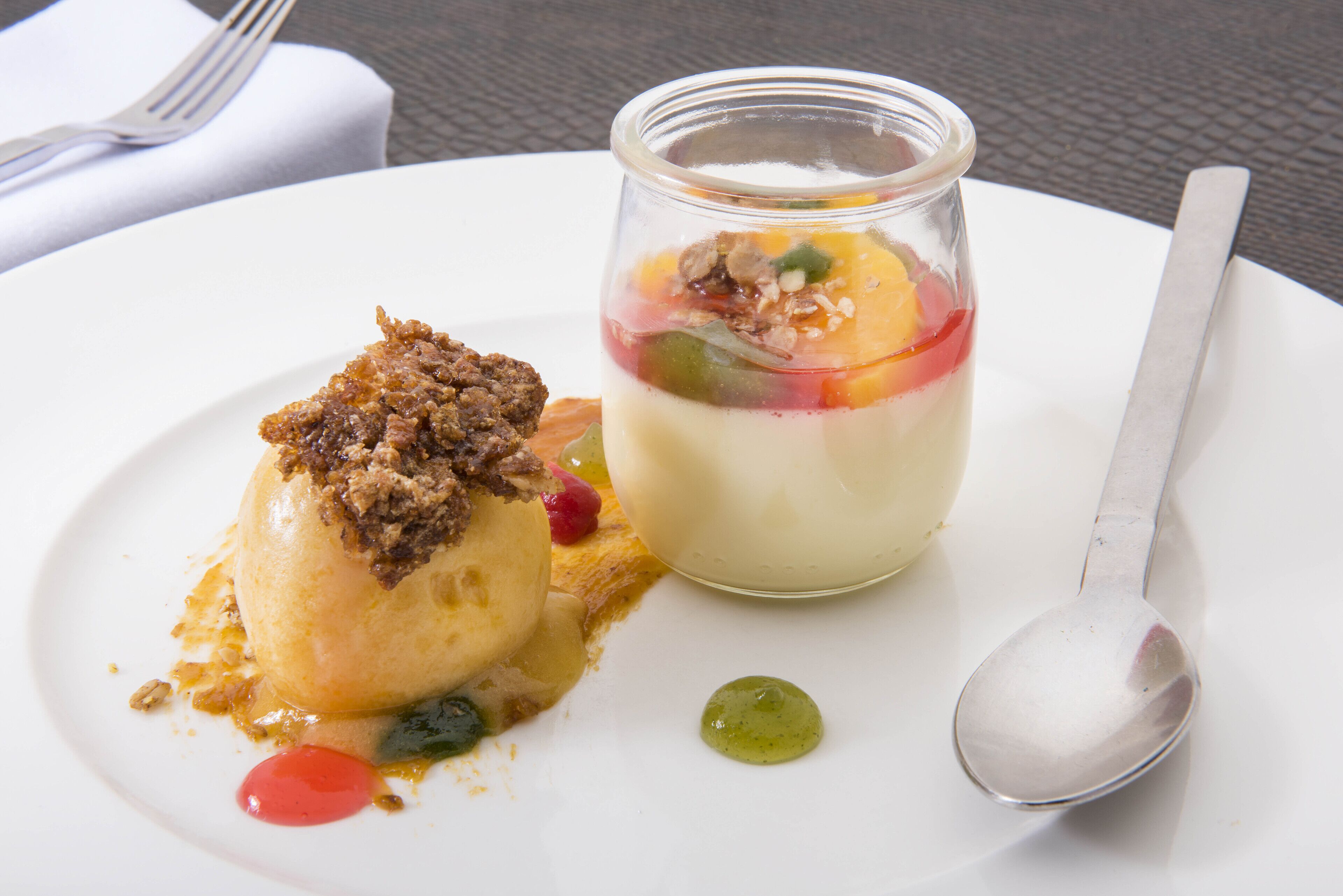 Een nagerechtenbord met een bolletje ijs en een glas gelaagde dessert.