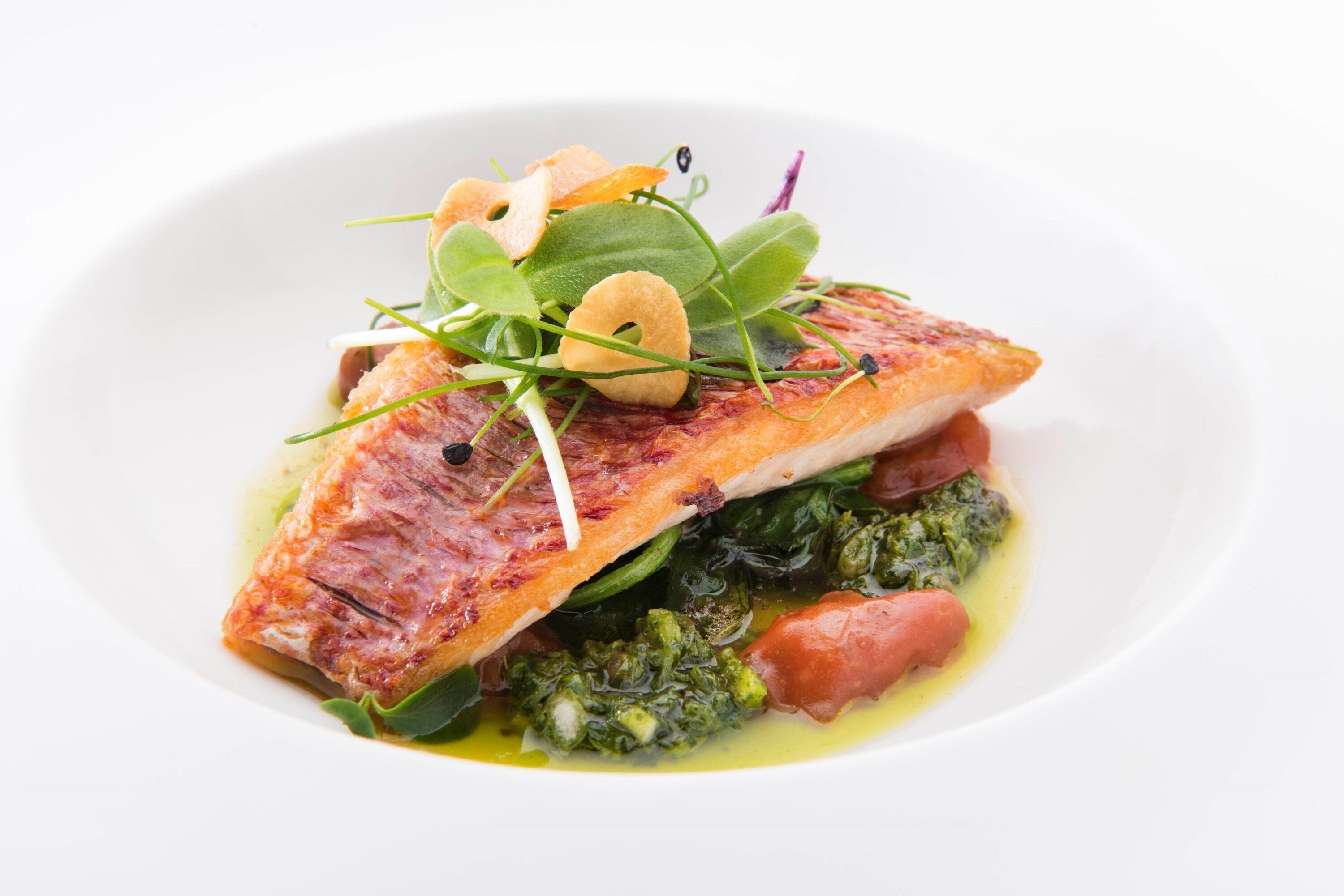 Prato com peixe, vegetais e tomate.
