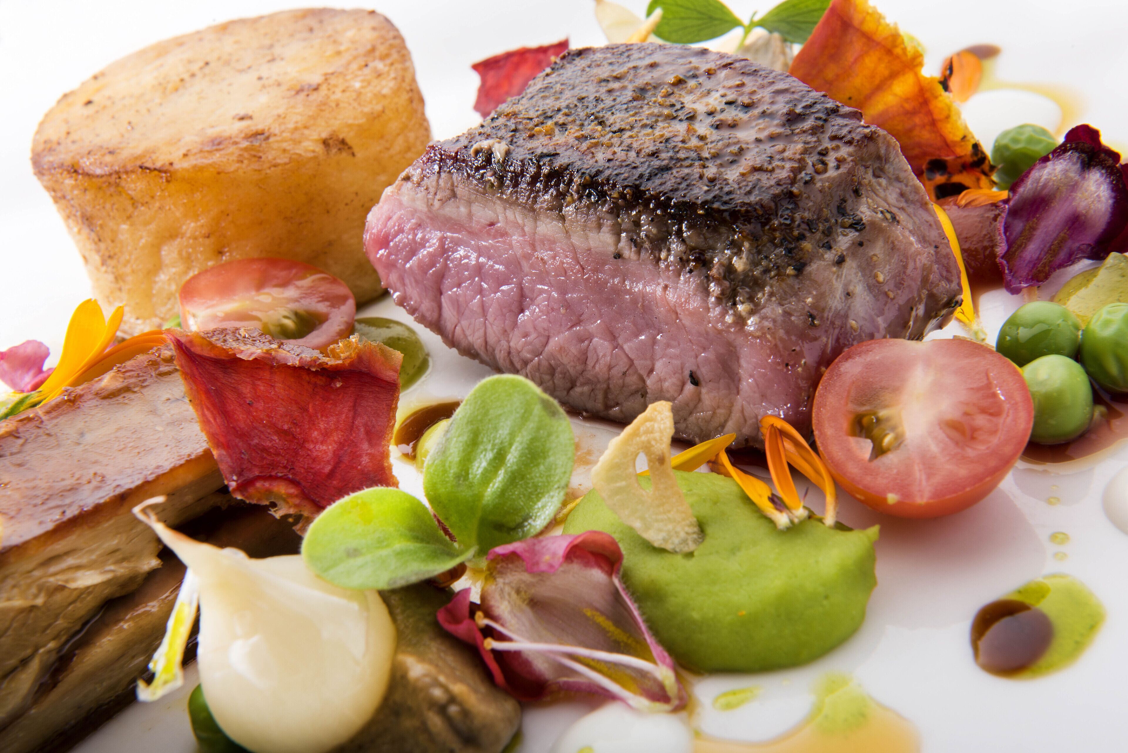 A steak with a crust, surrounded by vegetables and a small bowl.