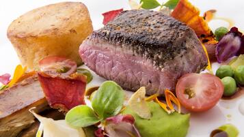 A steak with a crust, surrounded by vegetables and a small bowl.