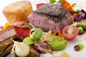 Un bistec con corteza, rodeado de verduras y un tazón pequeño.