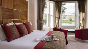 A hotel room with a large bed, red and beige bedding, a tray with a teapot and cups, and a view of a lake through the window.