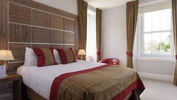 A hotel room with a large bed, wooden headboard, two bedside tables with lamps, a red chair, and a window with curtains.