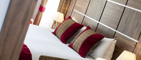 A neatly made bed with white linens and plaid pillows, a wooden headboard, and two bedside lamps.