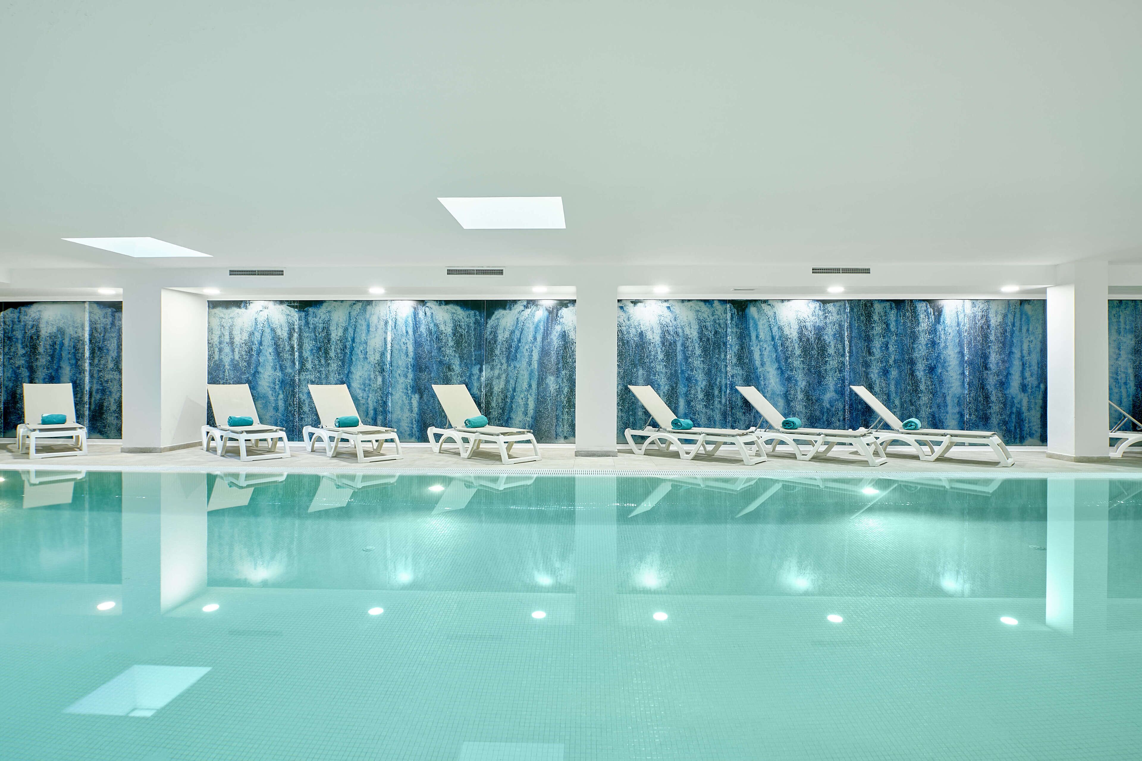 A swimming pool with lounge chairs and a blue mural wall.