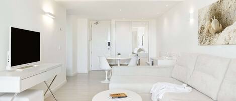 A modern living room with a flat-screen TV, a white sofa, a coffee table, and a dining area with a white table and chairs.