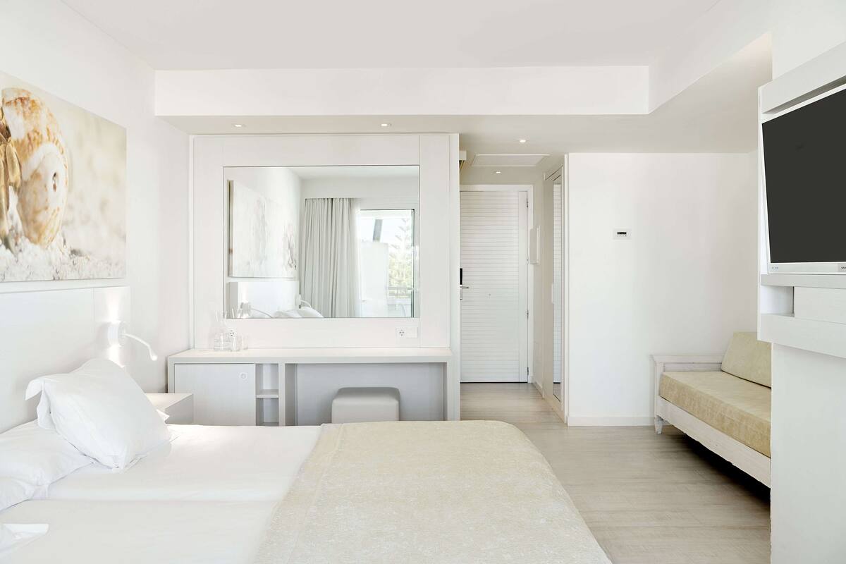 Ein modernes Hotelzimmer mit einem großen Bett, einem Schreibtisch mit Spiegel, einem Fernseher und einem Sofa.