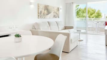 A modern living room with a white sofa, a round dining table, and a balcony with a view of trees.
