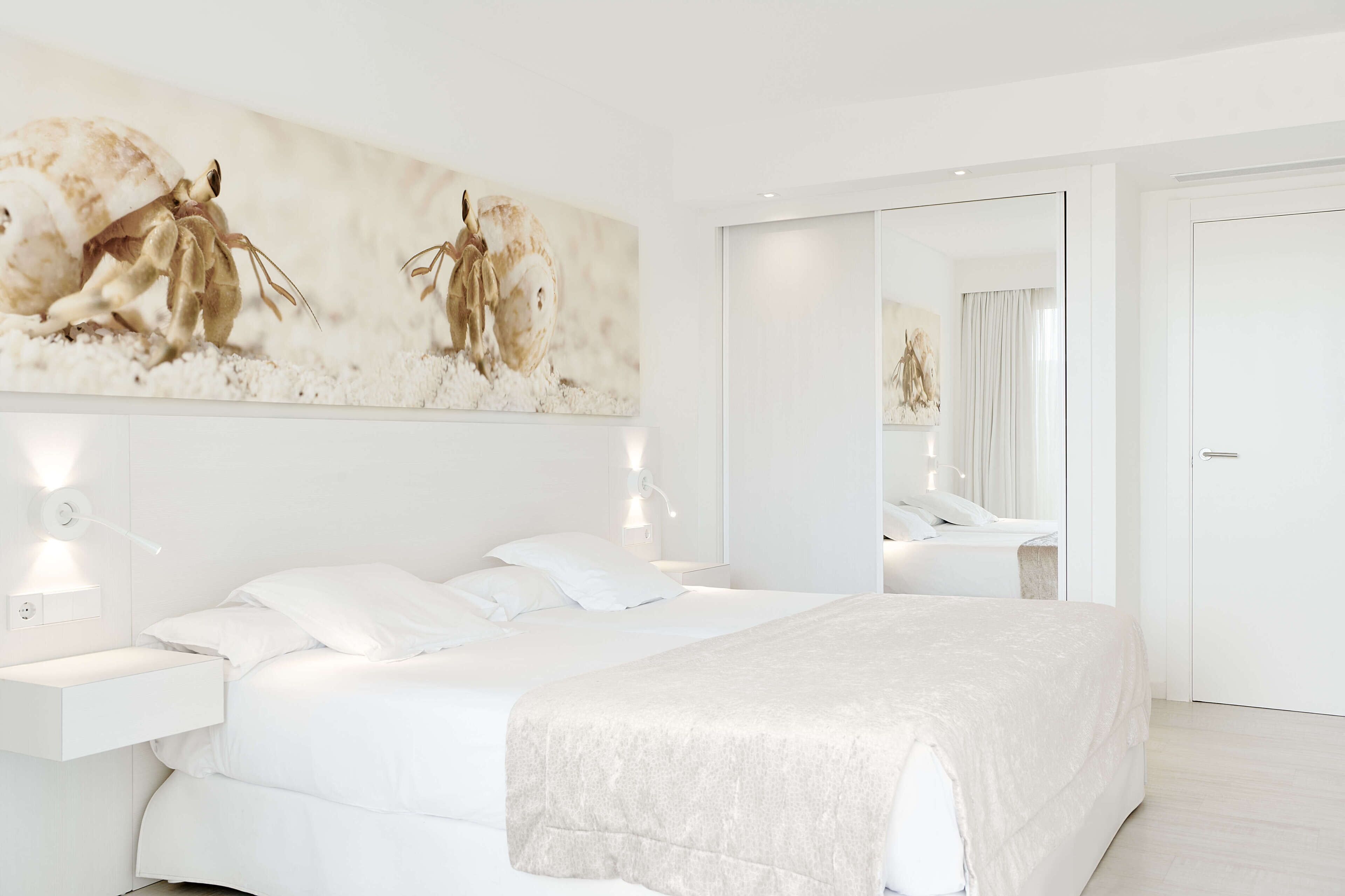 A modern bedroom with a large bed, bedside tables, a mirror, and a wall-mounted artwork.