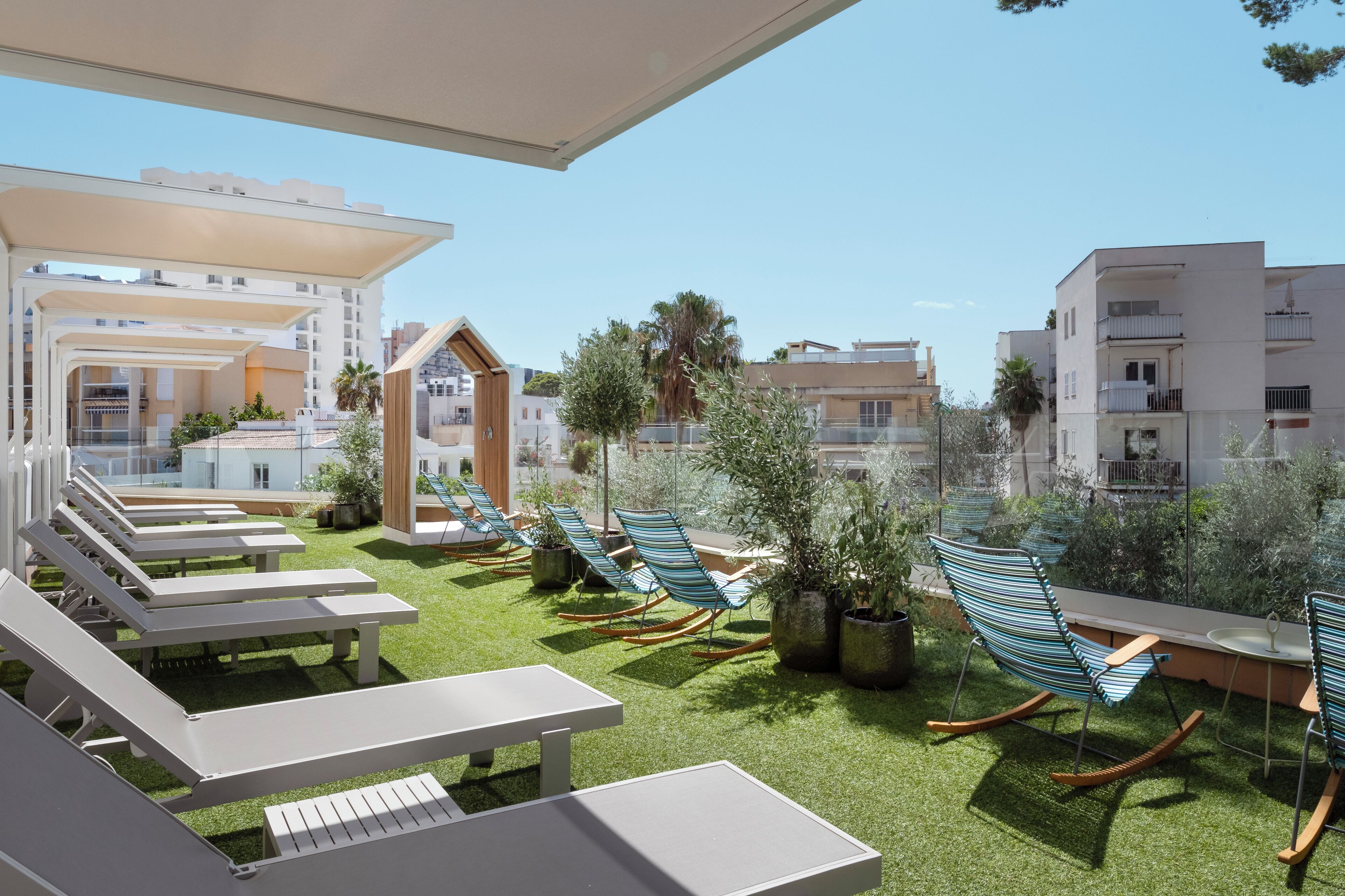 A rooftop terrace with white lounge chairs, a table, and potted plants.