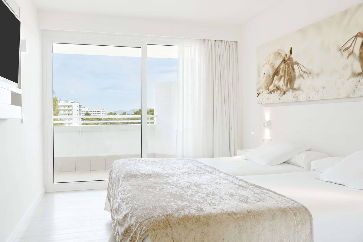 Ein Hotelzimmer mit Bett, einem großen Fenster mit Vorhängen und einem Bild an der Wand.