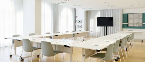 Un salón de conferencias con una larga mesa, sillas, un televisor de pantalla plana y un amplio ventanal con cortinas.
