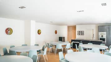 Una sala de conferencias moderna con mesas redondas y sillas azul claro, una zona de cocina con un refrigerador de marca y decoración en las paredes.