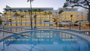 A hotel with a swimming pool, palm trees, and a multi-story building with balconies.