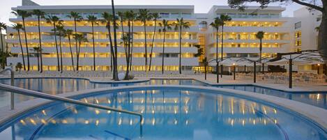 A hotel with a swimming pool, palm trees, and a multi-story building with balconies.