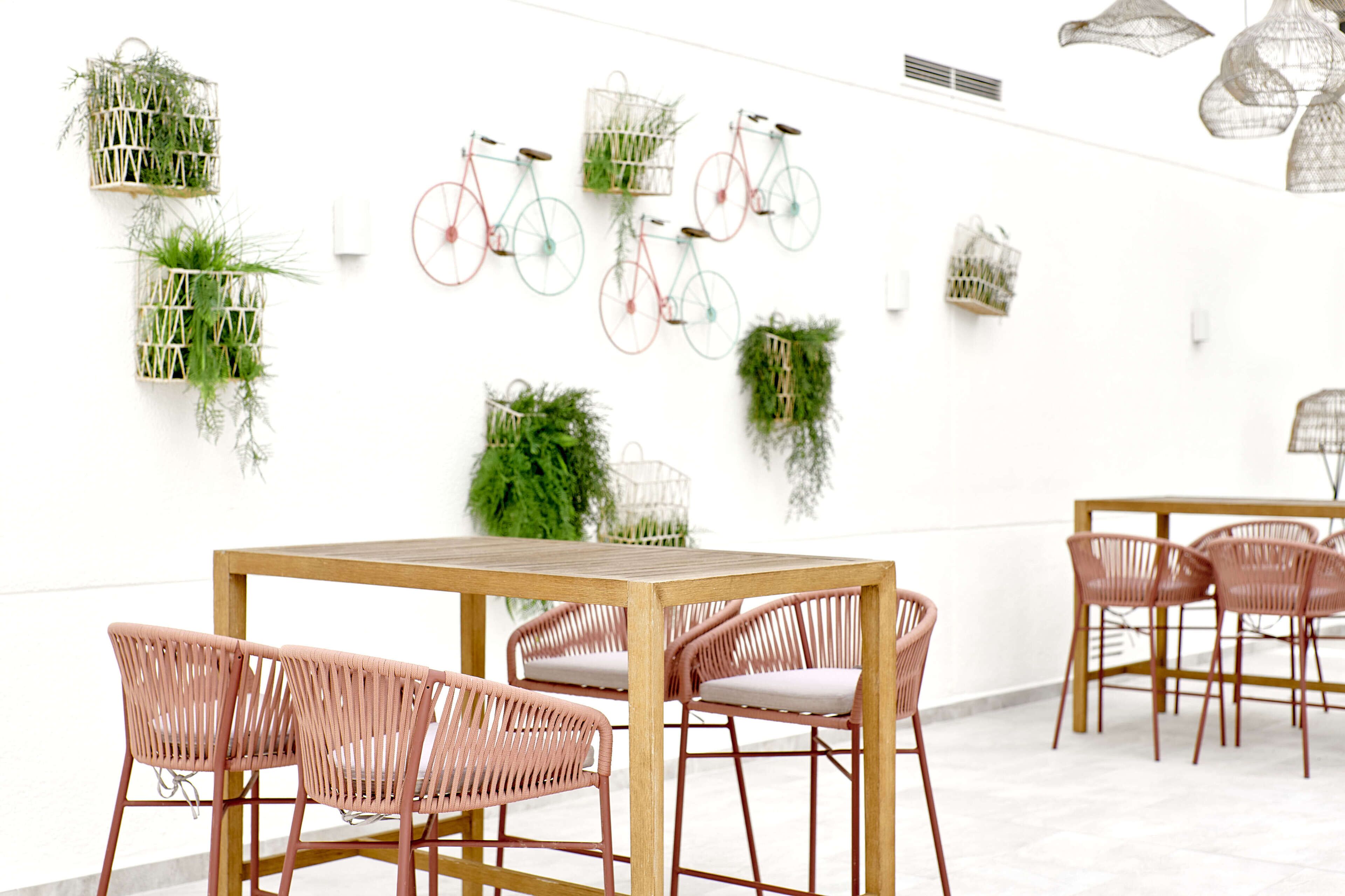 Een modern interieur met een houten tafel en rieten stoelen, omringd door planten en decoratieve fietsen.