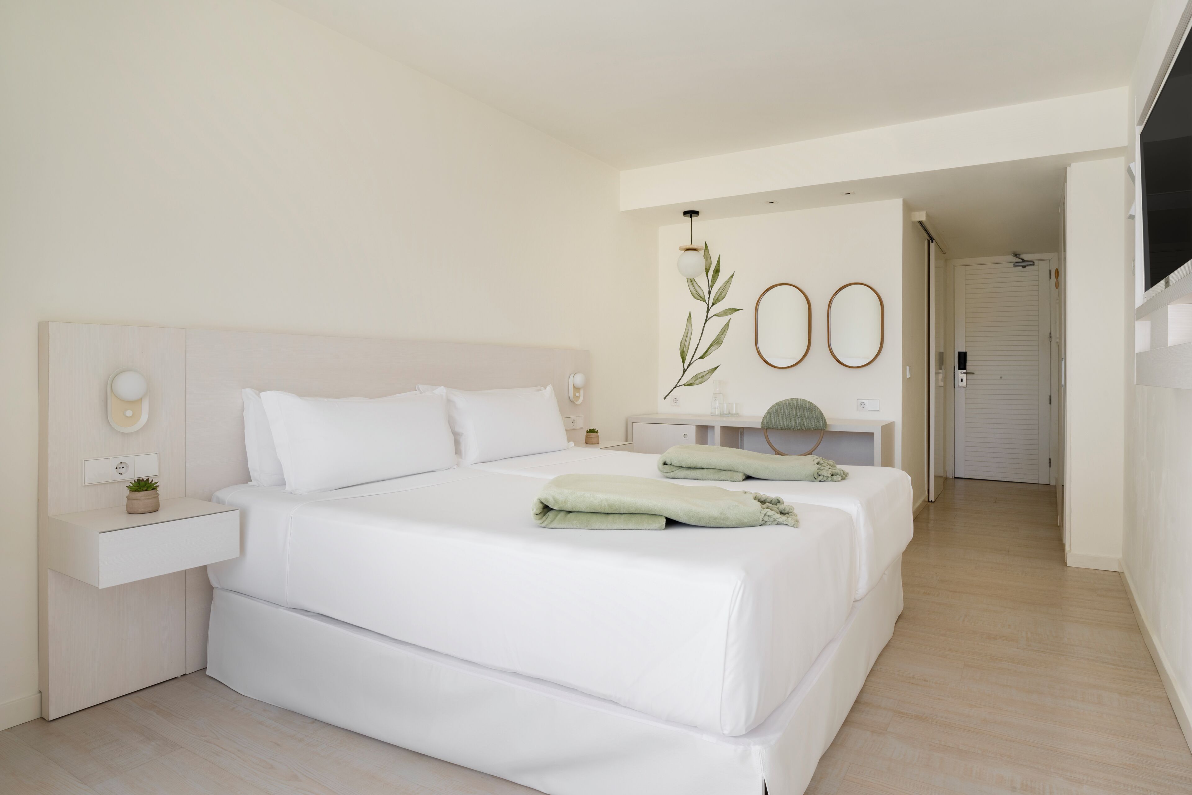 A modern bedroom with a large bed, bedside tables, a mirror, and a small plant.