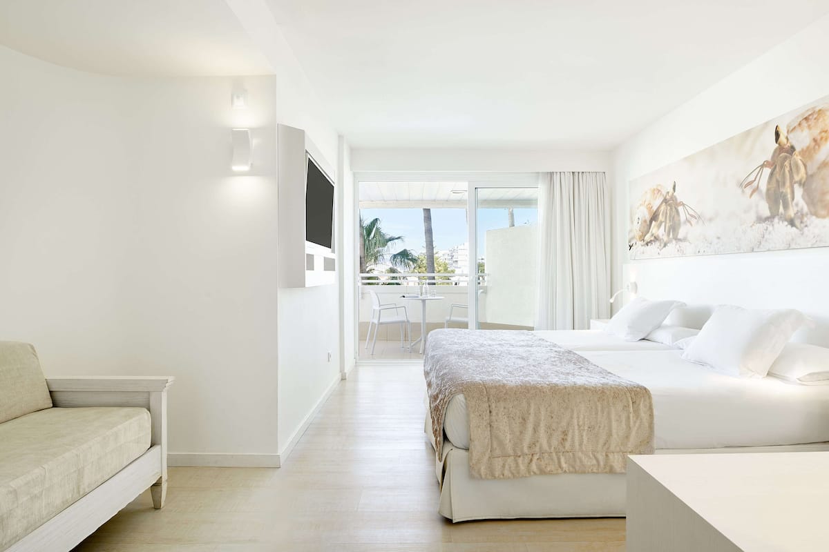 Ein Hotelzimmer mit Bett, einer Couch, einem an der Wand befestigten Fernseher und einem Balkon mit Tisch und Stühlen.