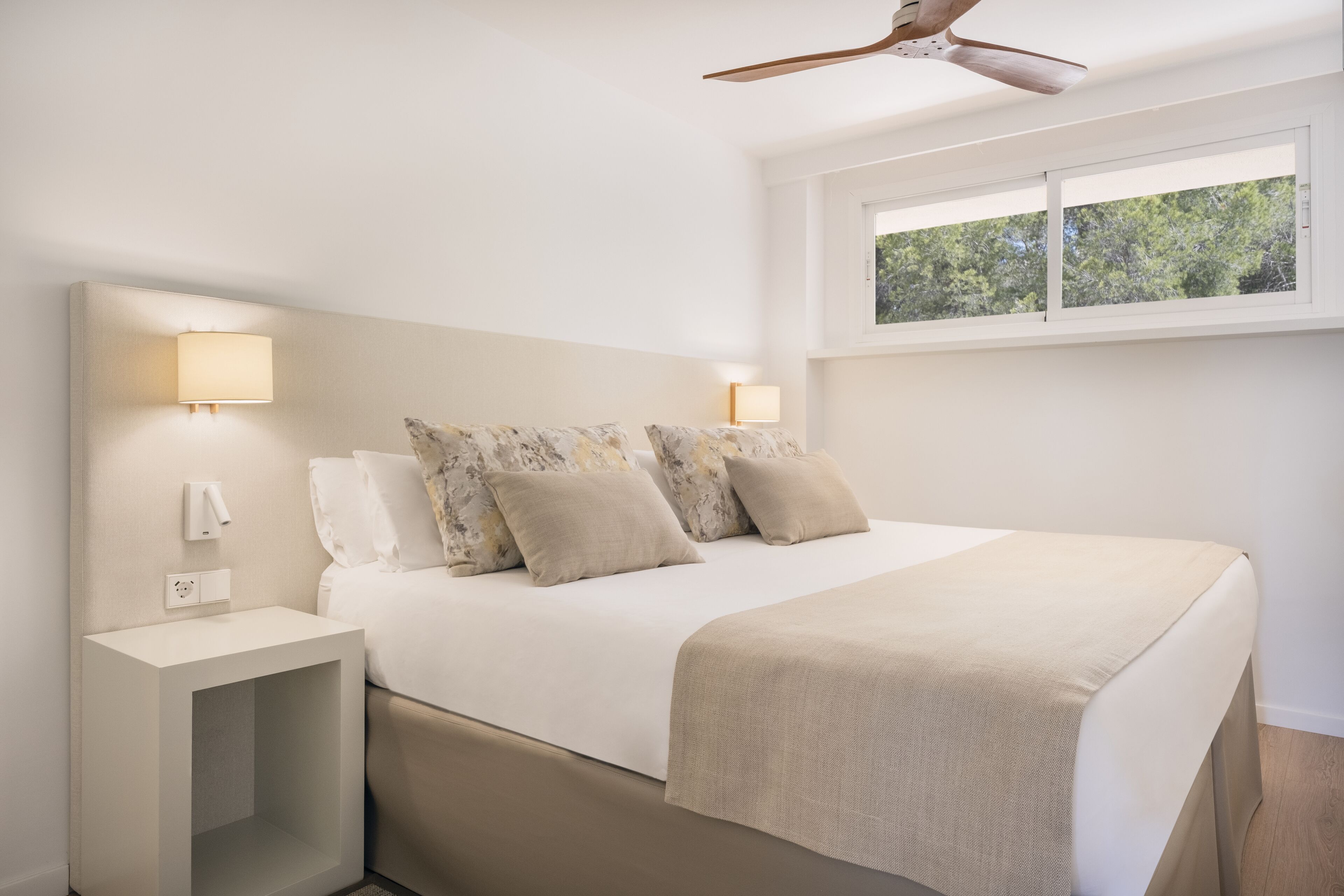 A modern bedroom with a bed, bedside lamps, a nightstand, and a ceiling fan.