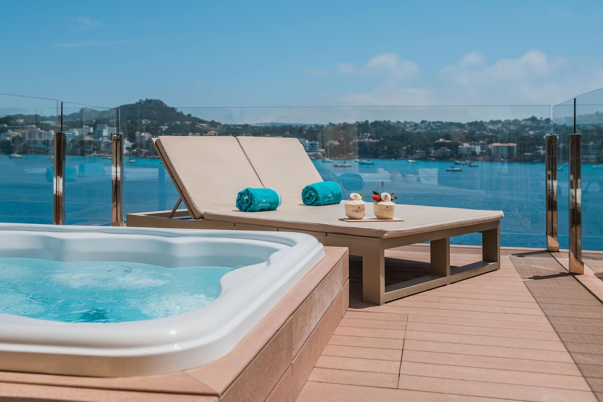 Een hottub en ligstoelen op een terras met uitzicht op een baai en gebouwen.