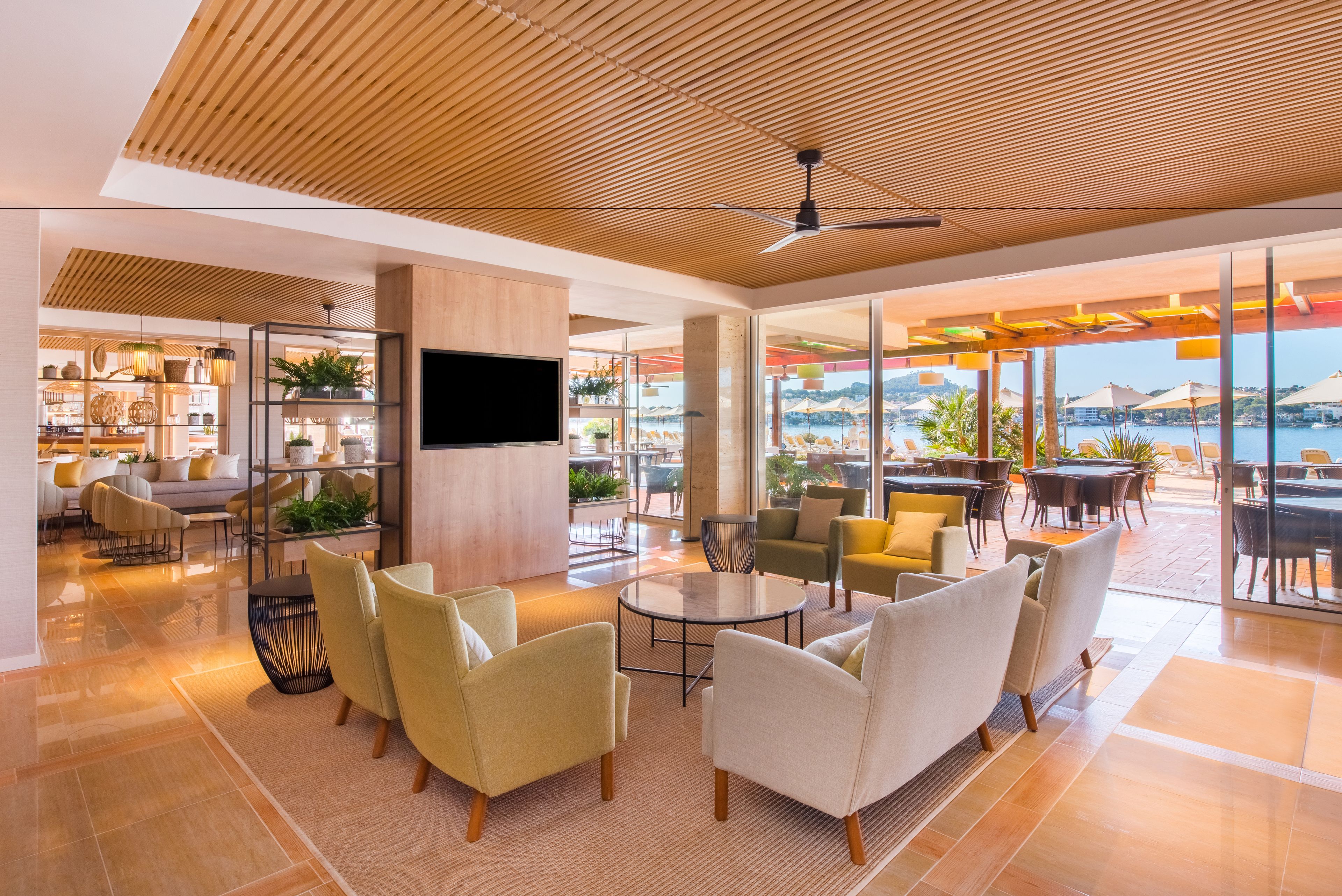 Un'ampia hall con un design moderno, caratterizzata da un soffitto in legno, comodi posti a sedere, una televisione e vista mare.