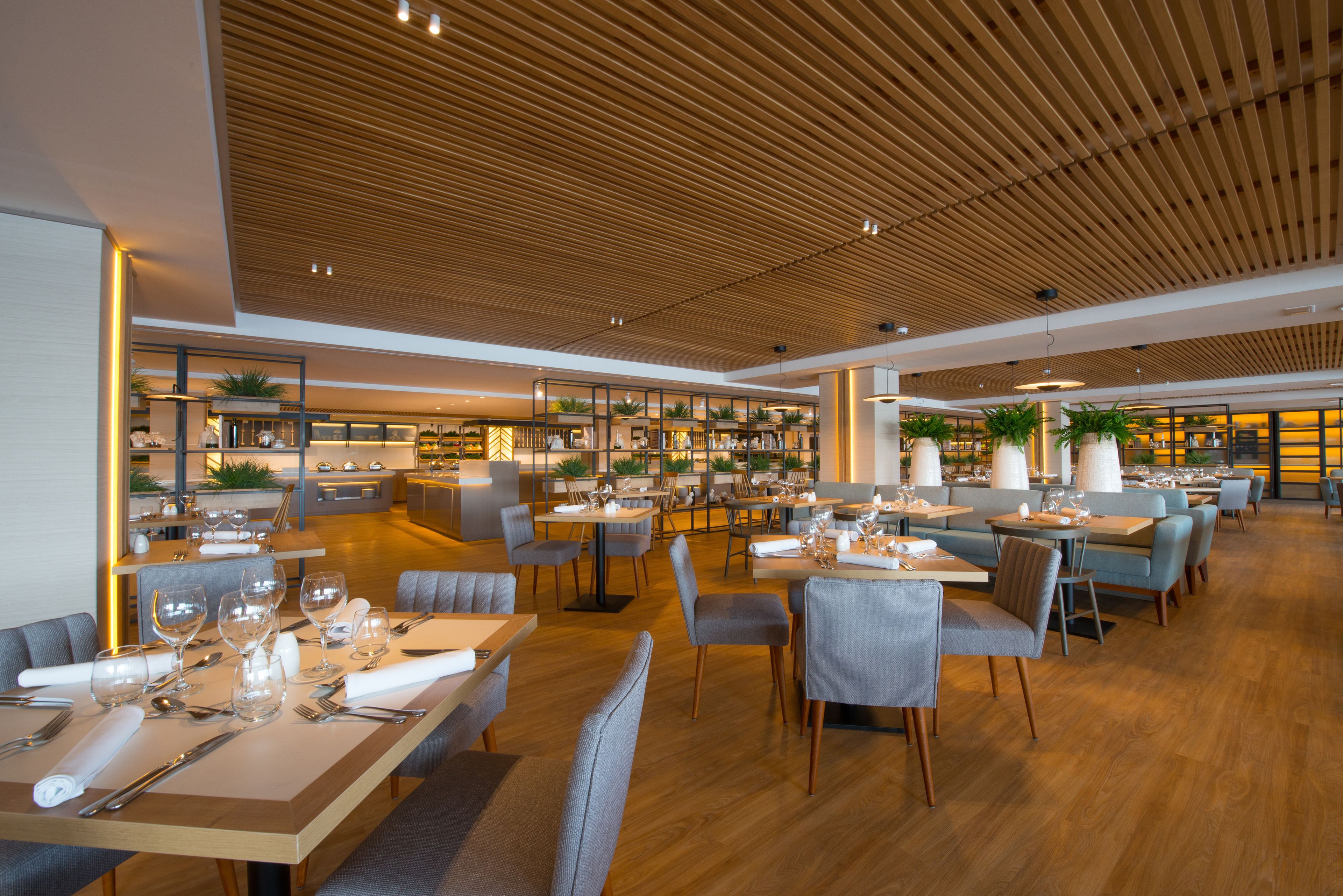 A modern restaurant with wooden ceiling, multiple dining tables, and comfortable seating.