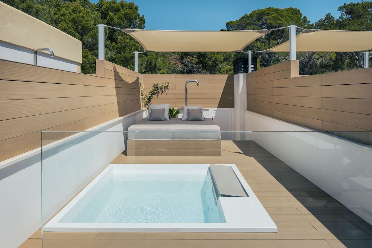 Een modern buitenzwembad met een glazen hottub, een houten terras en een zonnescherm voor schaduw.