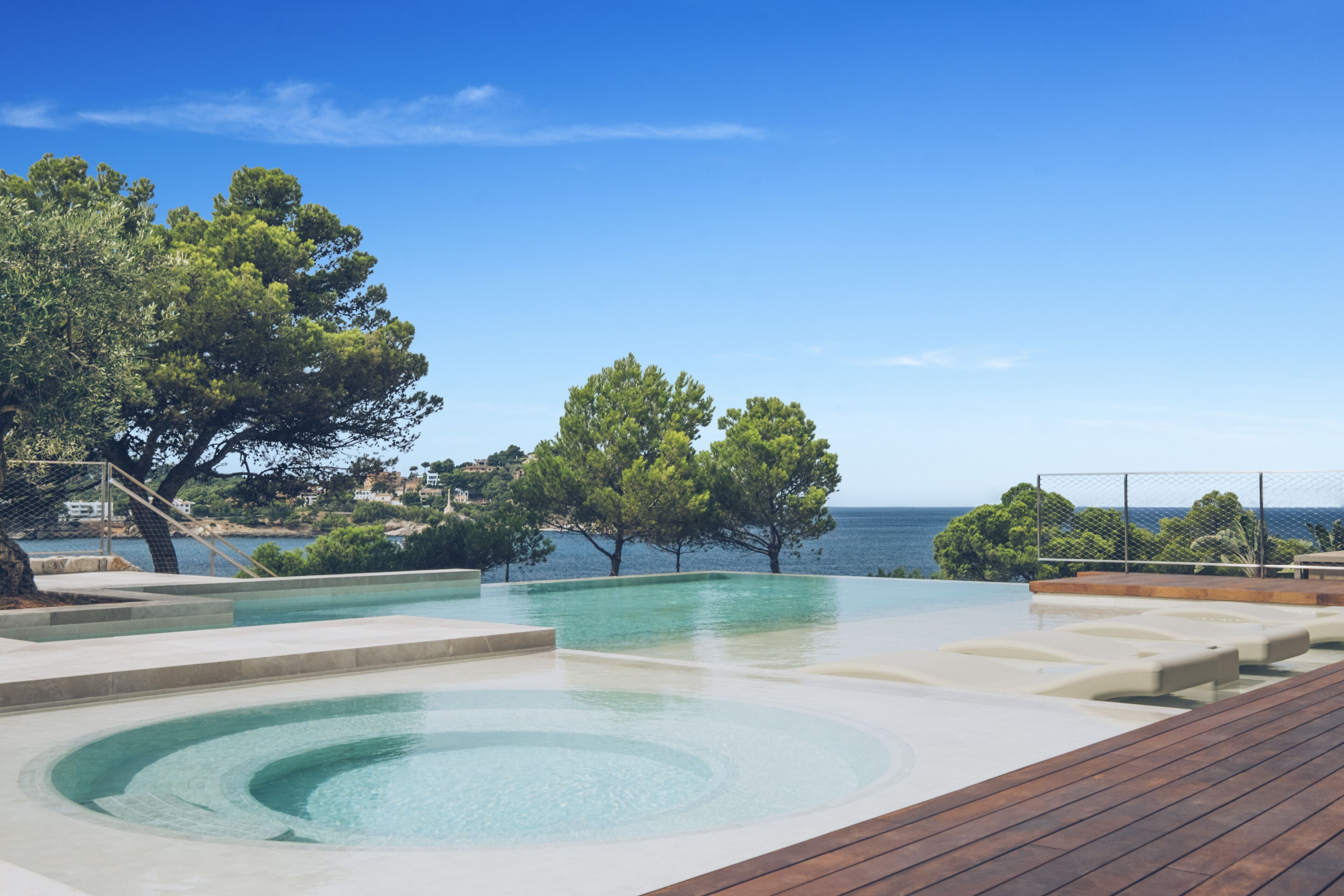 Ein Poolbereich mit Holzterrasse, blauem Himmel und Bäumen.