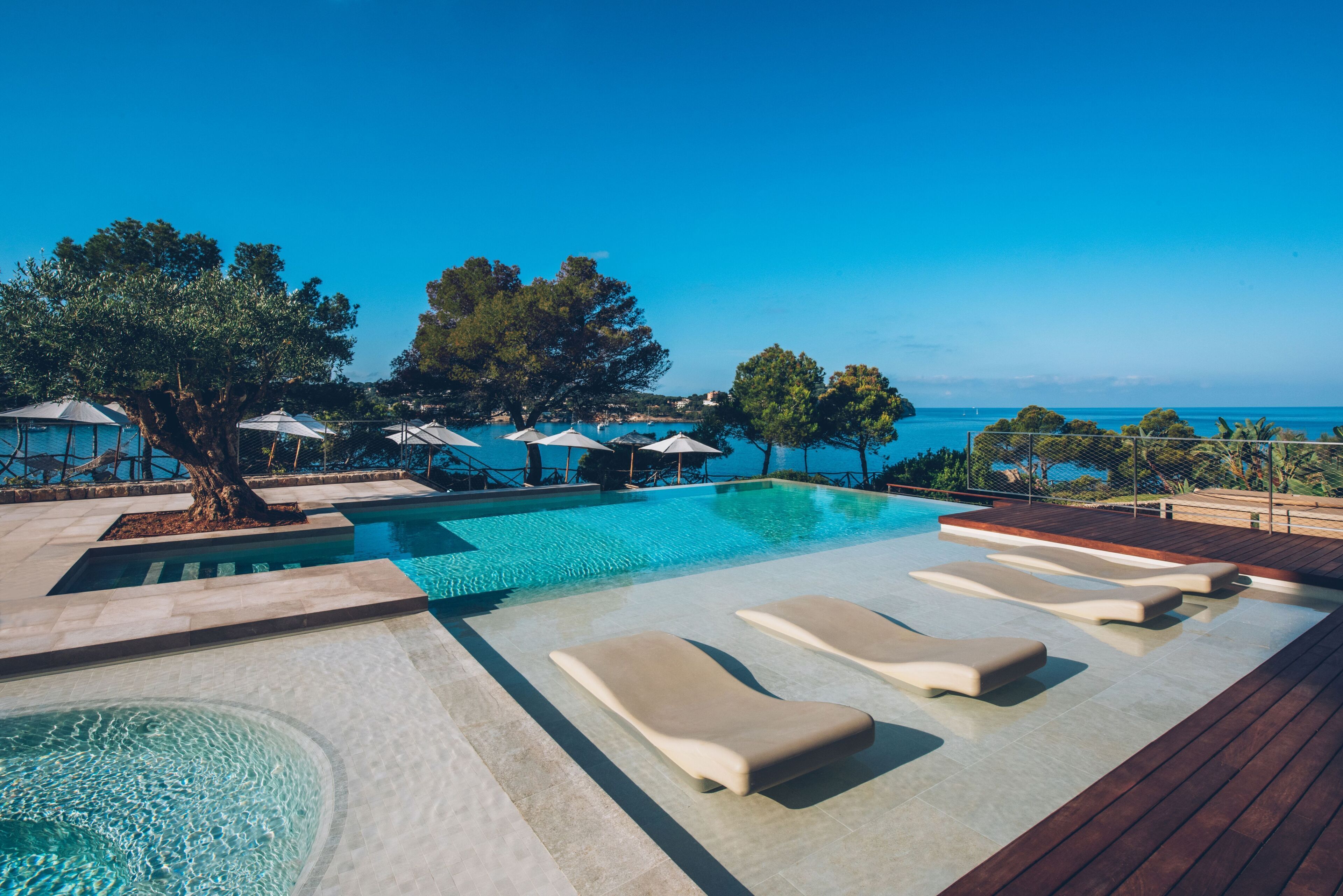 Zona de piscina con sillas de descanso, sombrillas y vistas al mar.