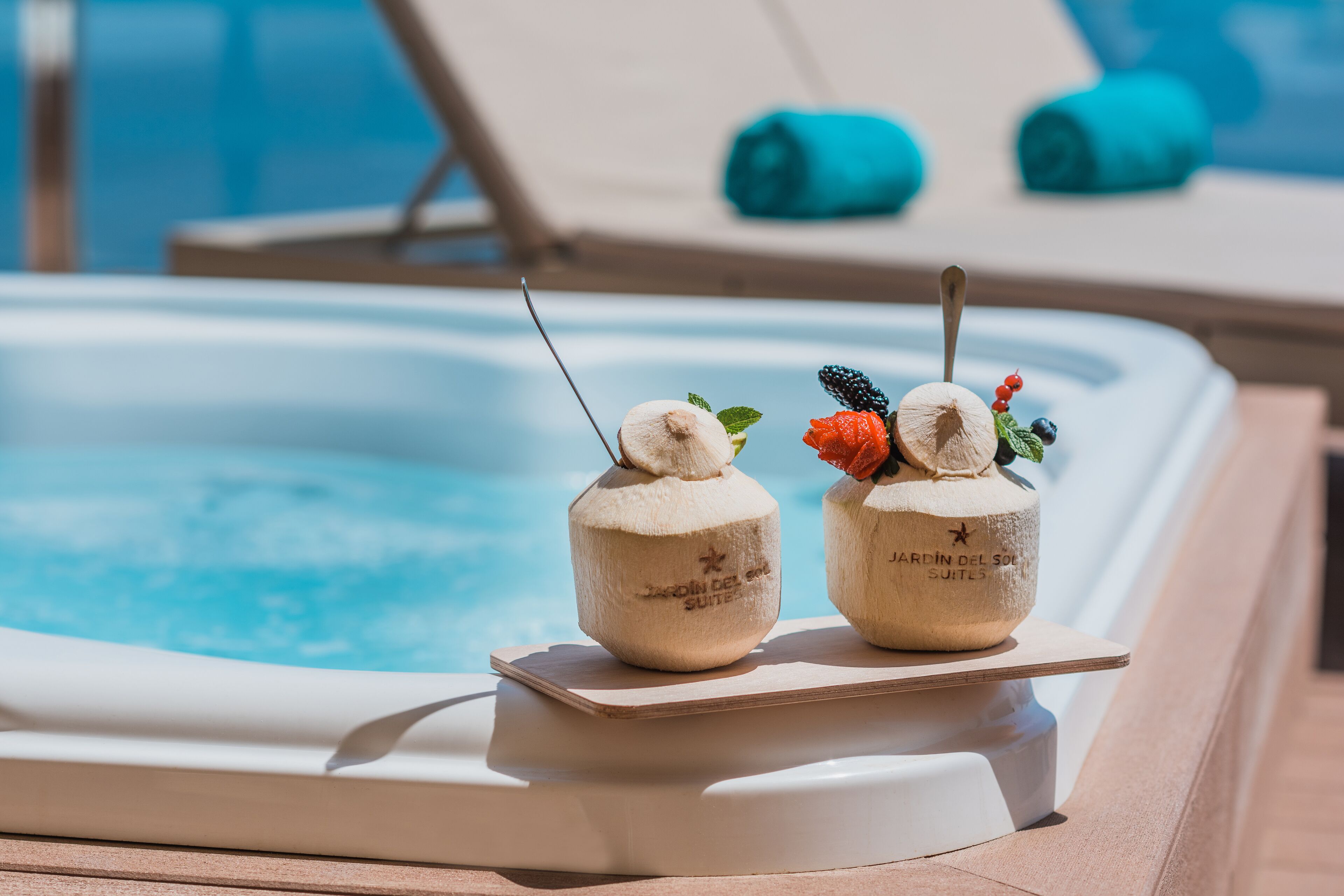 Two coconut-shaped drinks with garnishes on a poolside table.