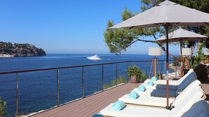 A deck with sun loungers, a potted plant, and a view of the sea and a boat. - Iberostar Selection Jardín del Sol Suites - Adults Only (Calvia)