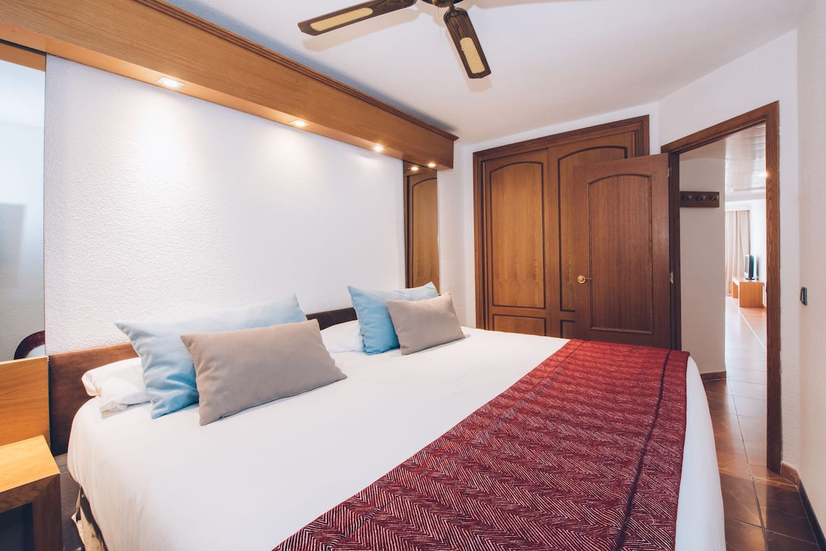 Een hotelkamer met een groot bed, een houten hoofdeinde, een plafondventilator en een rood beddegoed met een patroon.