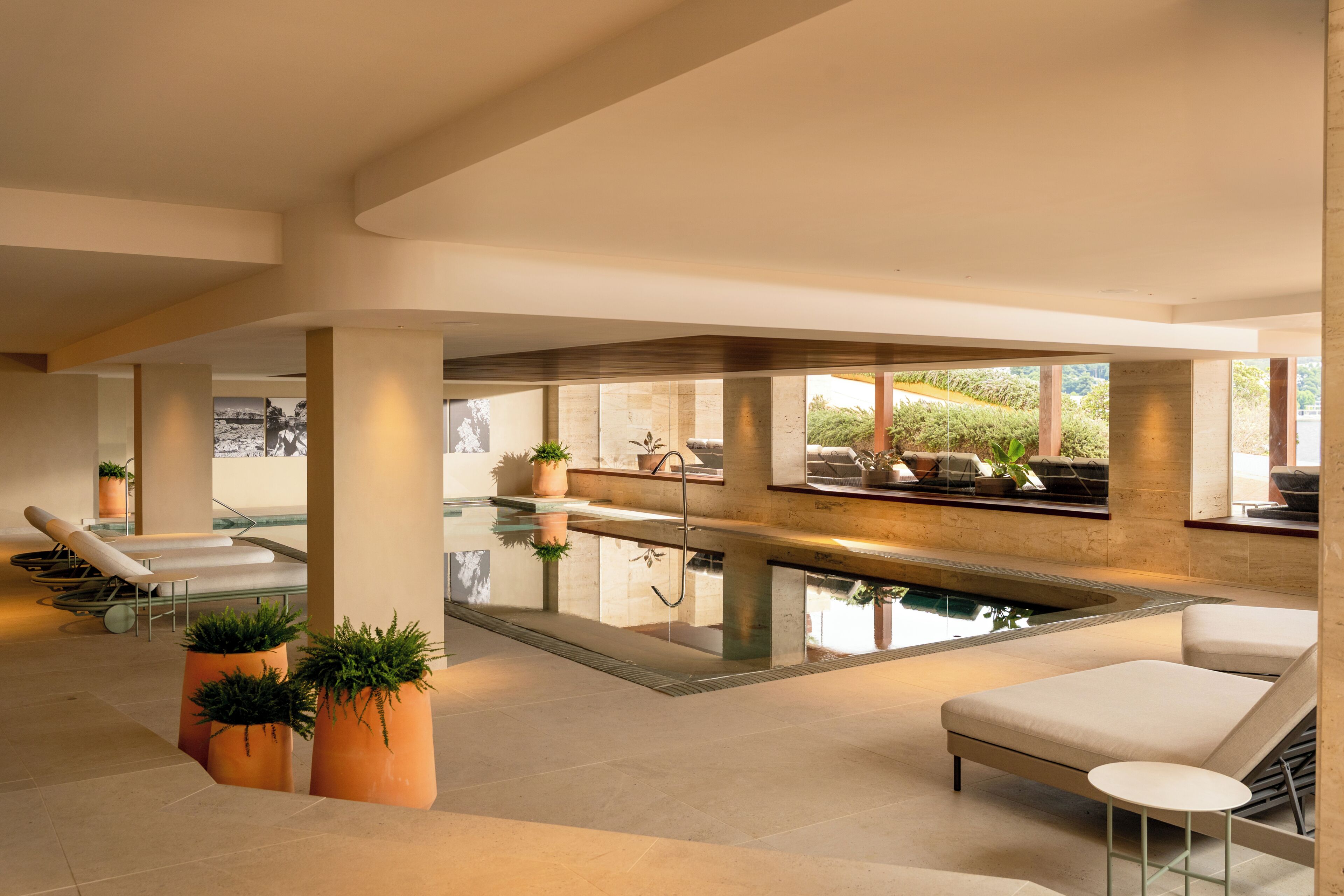 A modern indoor pool area with lounge chairs, a hot tub, and large windows.