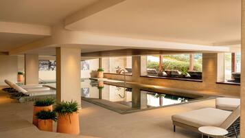 A modern indoor pool area with lounge chairs, a hot tub, and large windows.