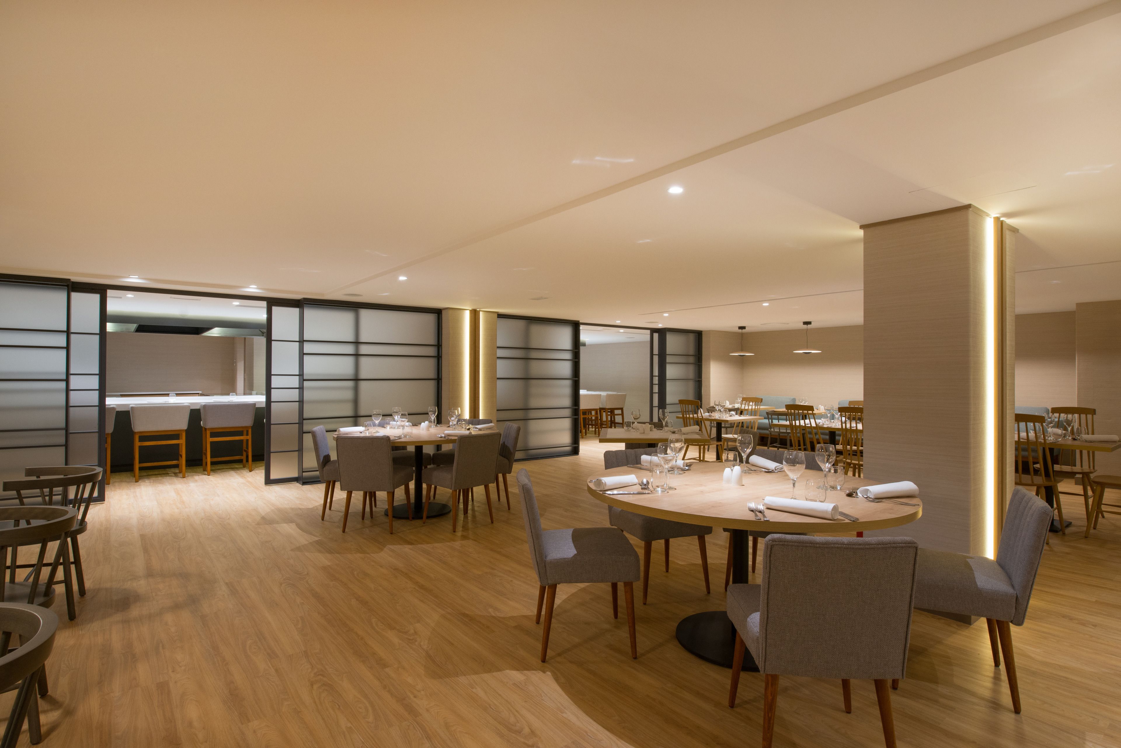 A spacious dining area with round tables and chairs, wooden flooring, and recessed lighting.