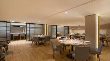 A spacious dining area with round tables and chairs, wooden flooring, and recessed lighting.
