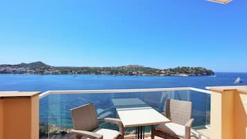 Un balcon avec des fauteuils en osier et une table, offrant une vue sur la côte, avec des bateaux et des bâtiments.