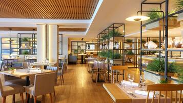 A modern restaurant with wooden flooring, multiple dining areas, and shelves with plants and kitchenware.