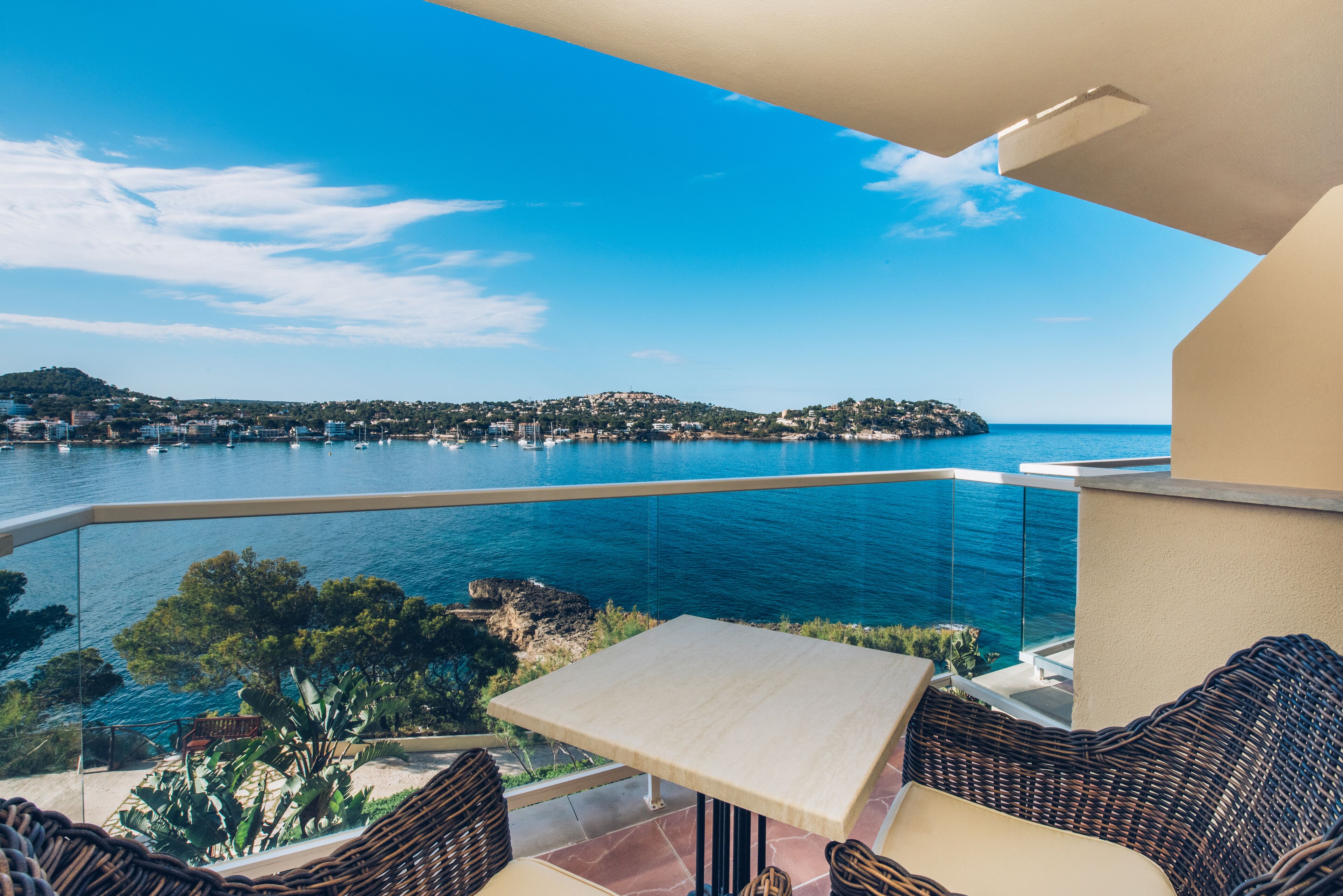 A balcony with a view of the sea, wicker furniture, and a table.