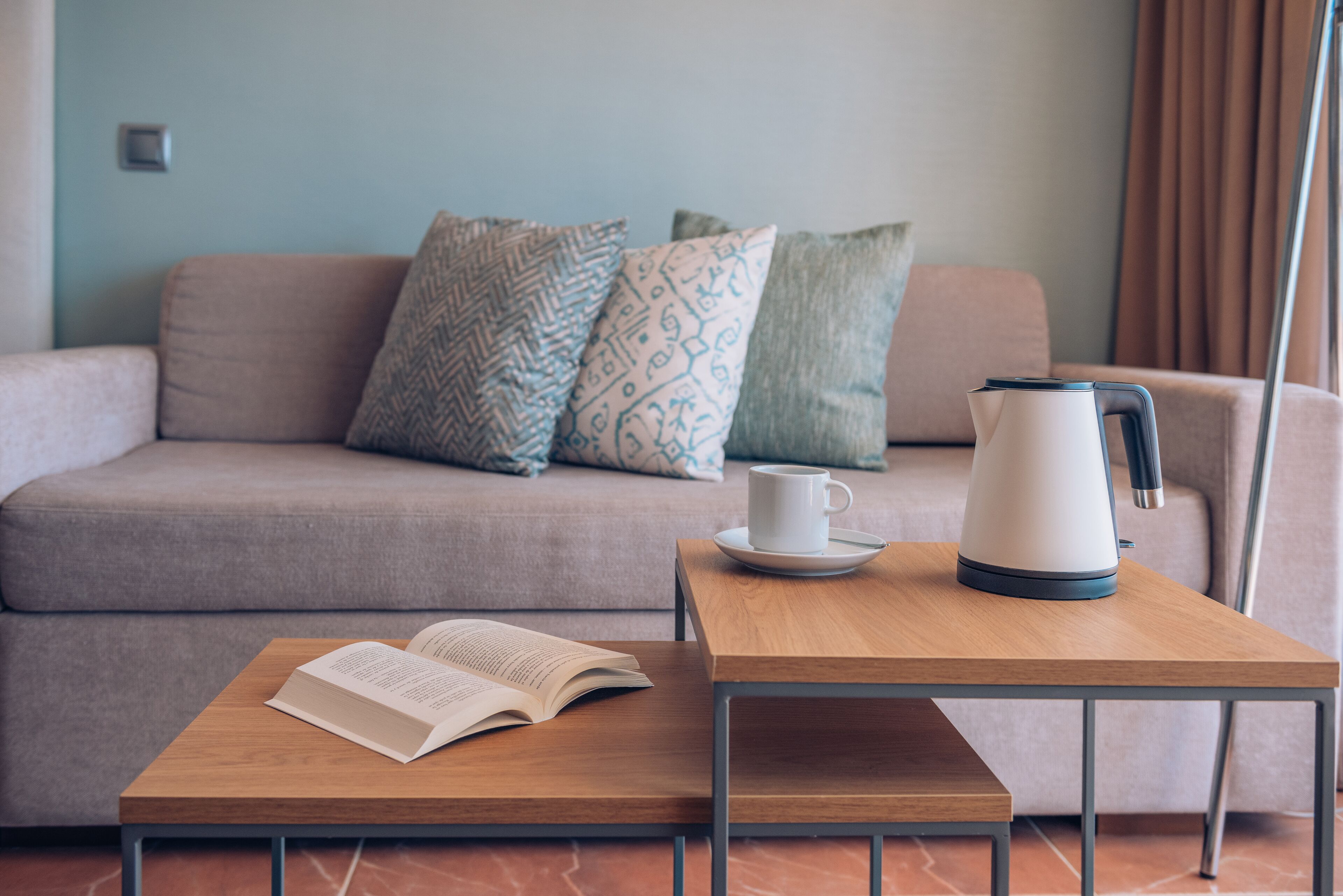 A modern living room with a sofa, a coffee table, a kettle, and an open book.