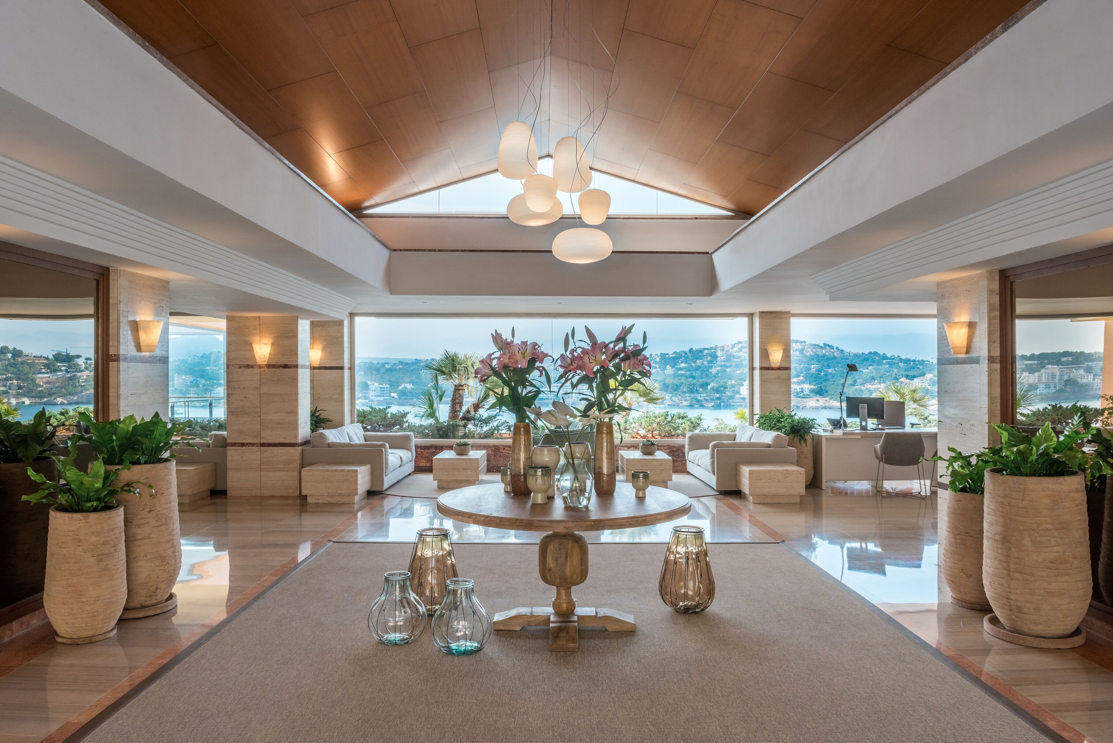 A spacious lobby with a high ceiling, a central round table, and large windows offering a city view.