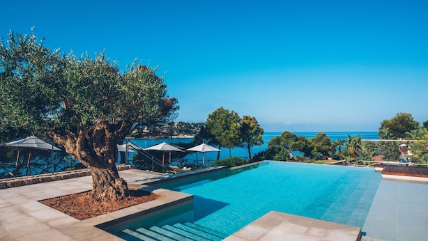 A swimming pool with a clear view of the sea, surrounded by trees and umbrellas. - Iberostar Selection Jardín del Sol Suites - Adults Only (Calvia)