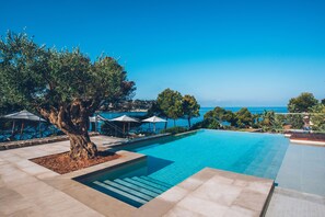 Une piscine offrant une vue dégagée sur la mer, entourée d’arbres et de parasols.