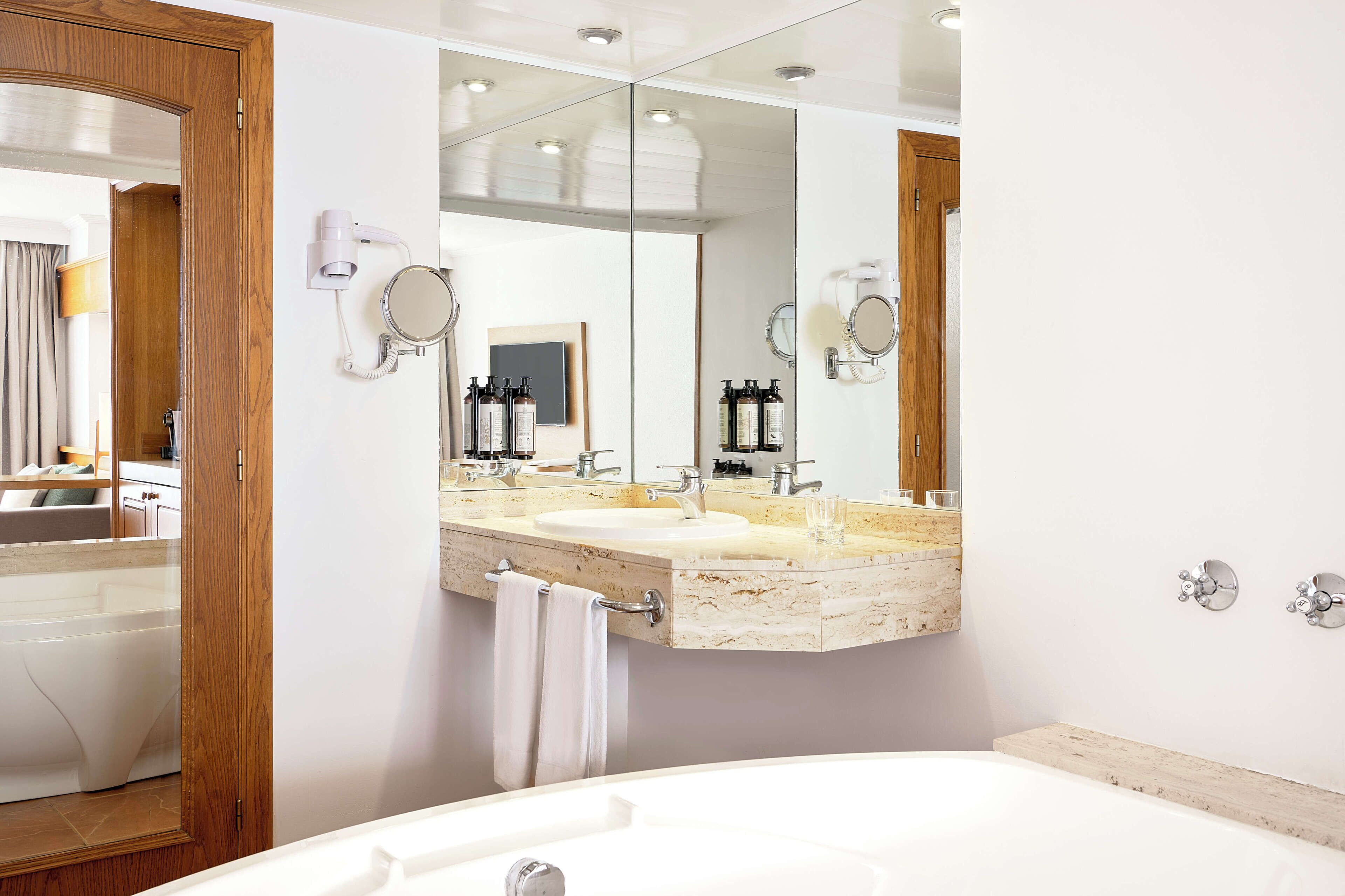 A modern bathroom with a large mirror, two sinks, a bathtub, and a towel rack.