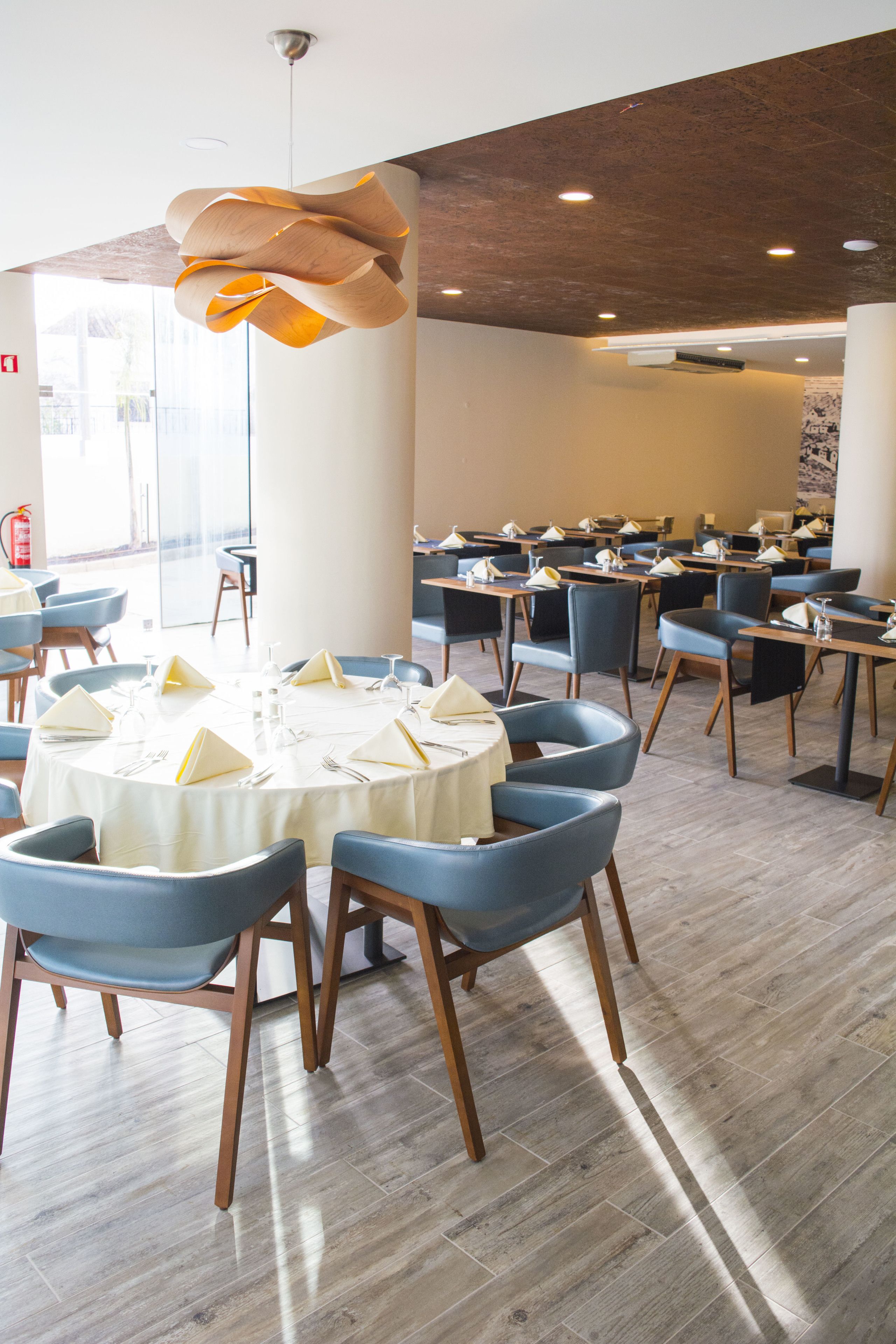 A dining area with round tables, blue chairs, and a modern pendant light.