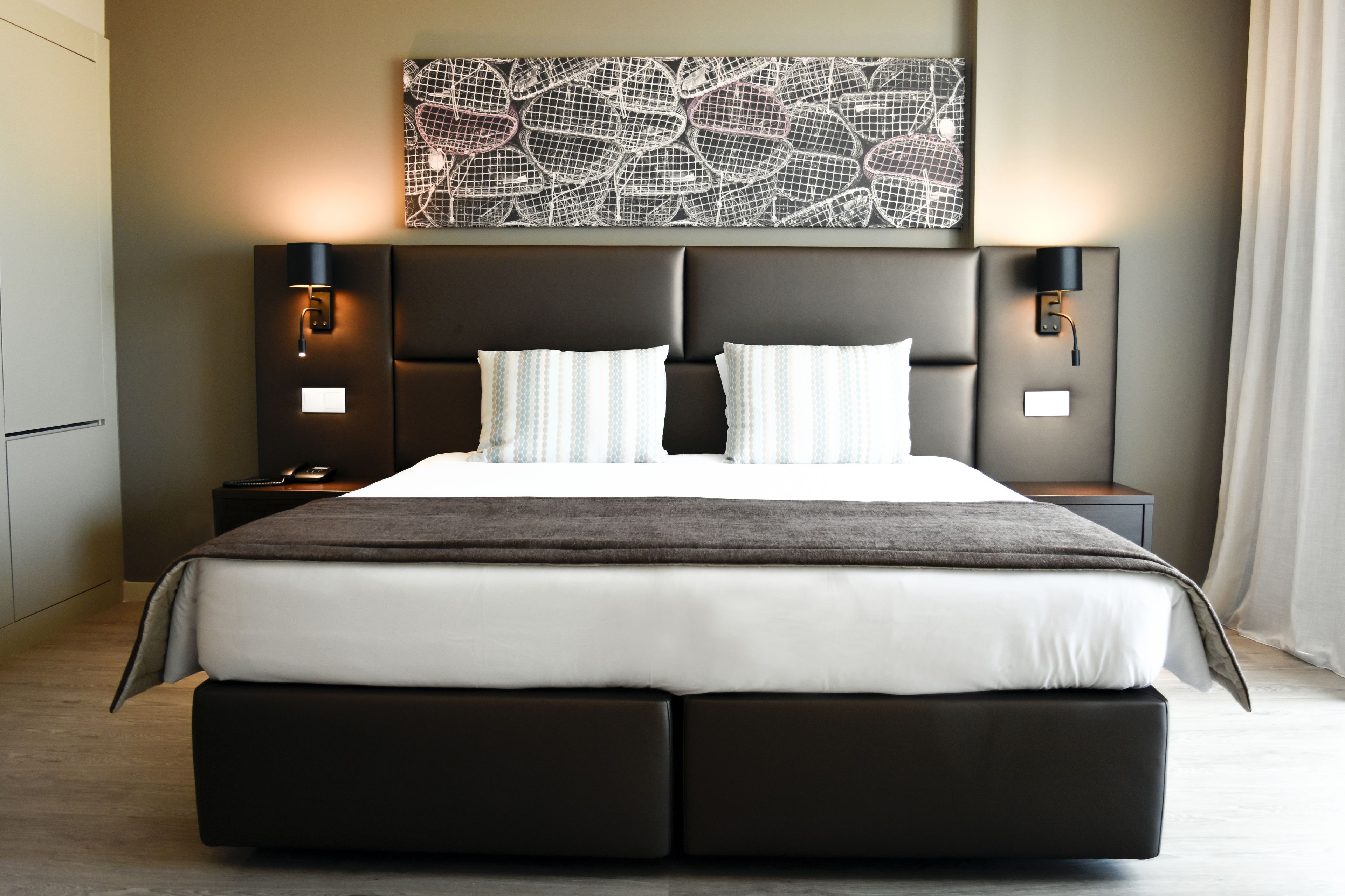 Ein modernes Hotelzimmer mit einem großen Bett, zwei Nachttischen und einem Wandbild.