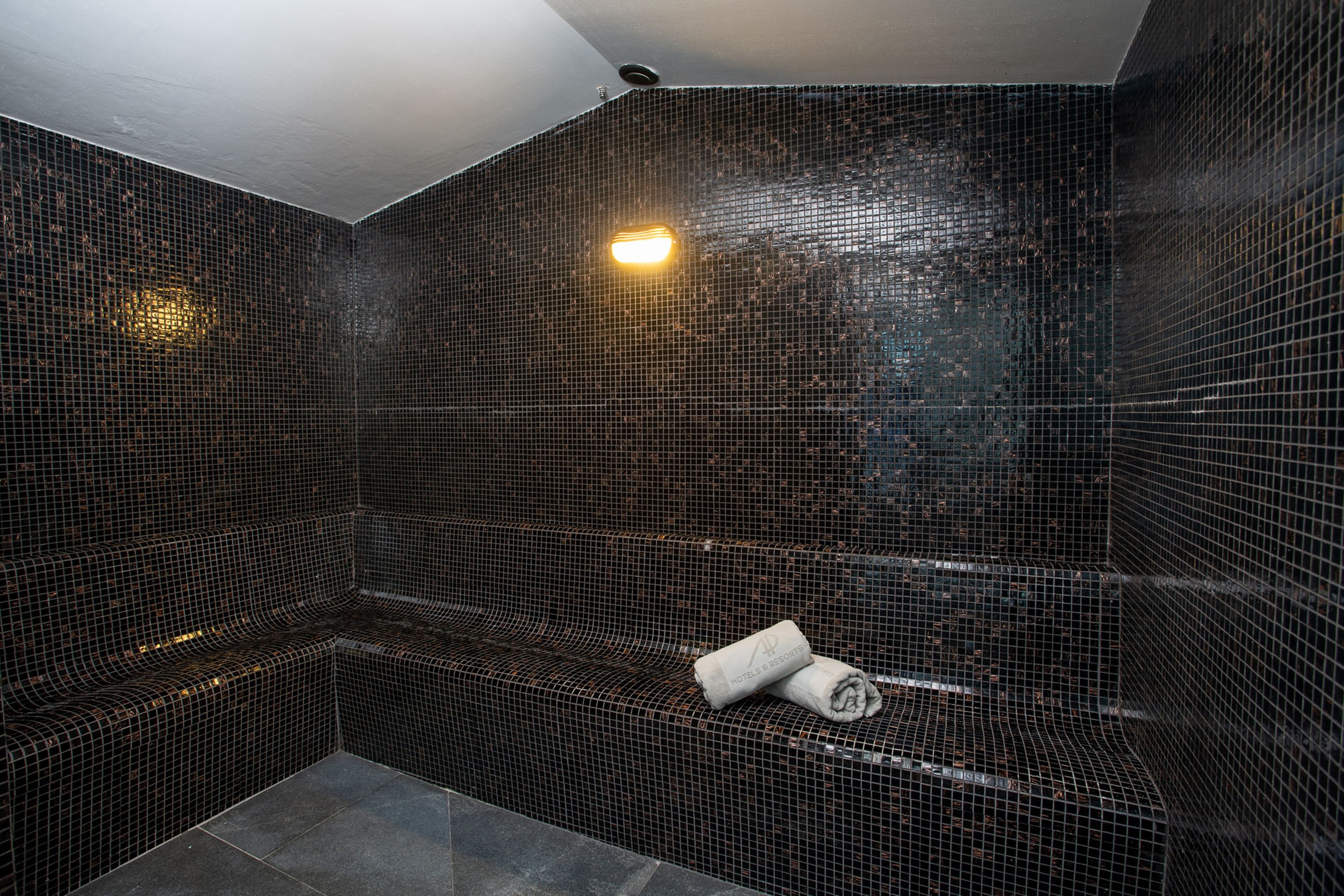 A tiled shower area with a bench and a towel.