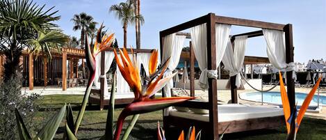 A poolside area with a wooden canopy bed, palm trees, and a pool.