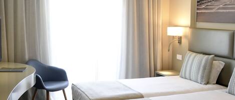 A hotel room with two beds, a desk, and a chair.