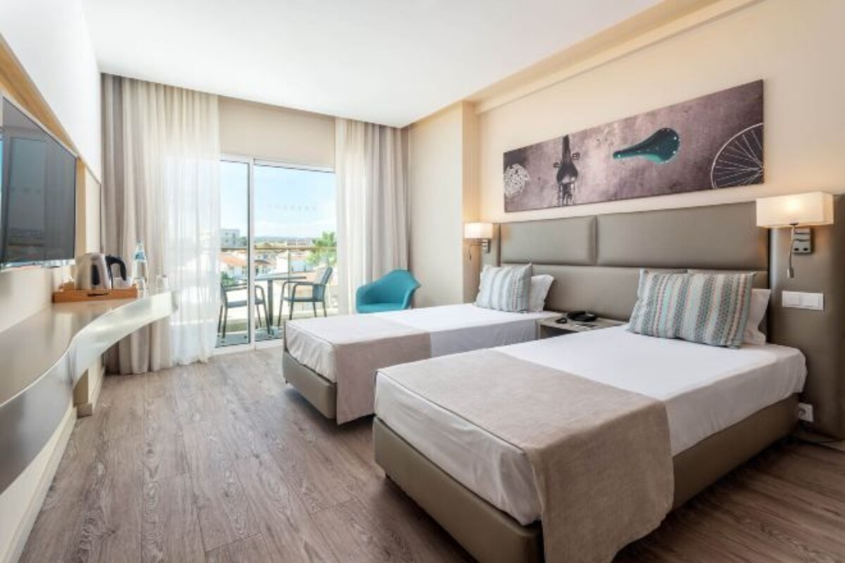 A hotel room with two beds, a TV, a desk, and a balcony with a view.